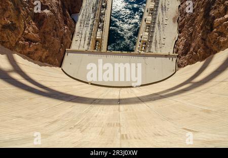 An overhead view down the dam's curved face to the power plant's flat roof and rushing white water below, Hoover Dam on the Nevada-Arizona border. Stock Photo