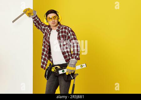 Worker man or builder in construction helmet near white banner on yellow background. building carpentry profession Stock Photo