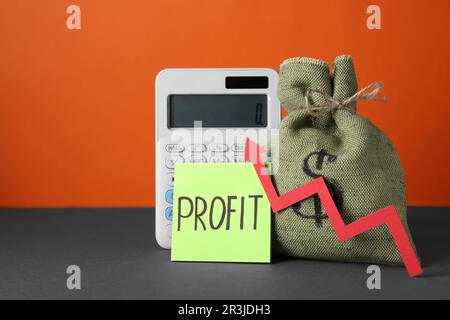 Economic profit. Money bag, calculator, note and arrow on grey table against orange background, space for text Stock Photo