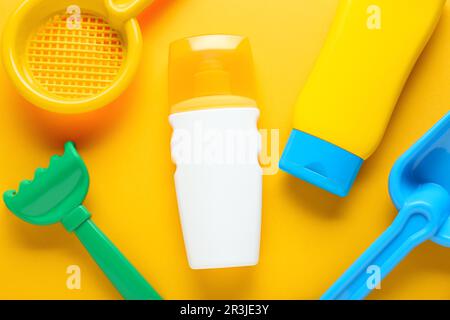 Different suntan products and plastic beach toys on orange background, flat lay Stock Photo