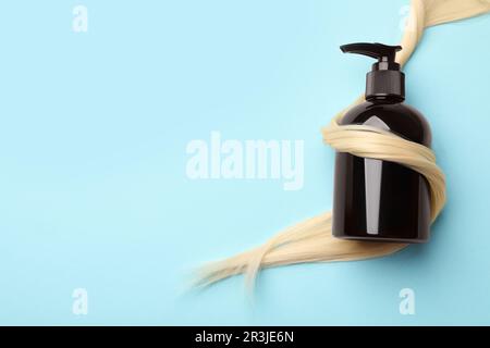 Shampoo bottle wrapped in lock of hair on light blue background, top view. Space for text Stock Photo