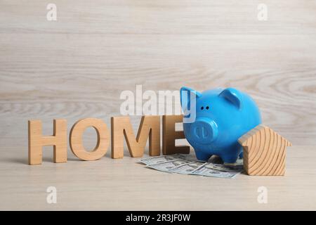 Piggy bank, house model, banknotes and word Home made of wooden letters on table Stock Photo