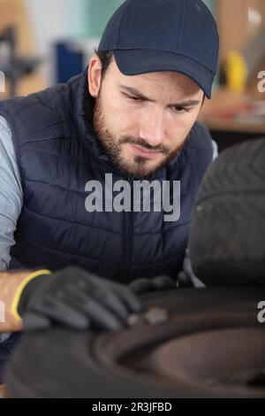 young mechanic with blue uniform checking black tyre Stock Photo