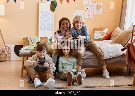 Full length portrait of diverse group of children playing videogames together and having fun Stock Photo