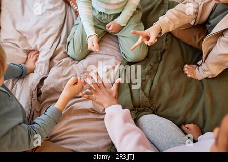 Top view closeup of group of kids playing rock paper scissors while sitting on bed in circle, copy space Stock Photo