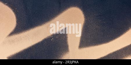 Messy paint strokes and smudges on old black painted wall. Light brown beige drips, flows, streaks of paint and paint sprays Stock Photo