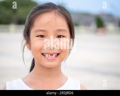 close up shot of face asian child cute or kid girl smiling eyes white teeth and one broken tooth or drop from baby or milk tooth on 7 years old Stock Photo