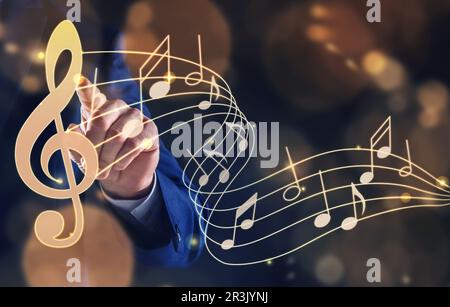 Musician pointing at staff with music notes and treble clef on color background, closeup Stock Photo