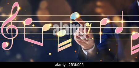 Musician pointing at staff with music notes and symbols on color background, closeup. Banner design Stock Photo