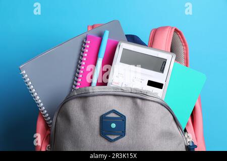 Backpack with different school stationery on light blue background Stock Photo