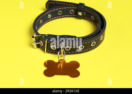 Black leather dog collar with golden tag in shape of bone on yellow background Stock Photo