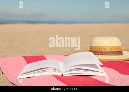 Open book, hat and striped towel on sandy beach near sea. Space for text Stock Photo