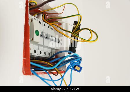 Switchboard with different cables on white wall. Installation of electrical wiring Stock Photo
