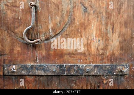 Fragment of an old wooden gate painted brown with a rusty metal plank and a locking hook close up view Stock Photo