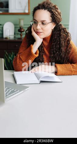 Contemplative Young Woman Taking Breaks from Online Learning and Working on Laptop at Home. Young Woman Studying and Working from Home, Lost in Stock Photo