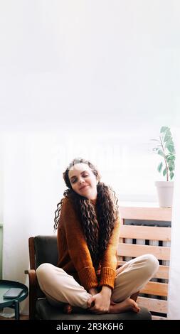 Young relaxed smiling pretty woman relaxing sitting on chair at home. Happy positive beautiful lady feeling joy enjoying wellbeing and lounge chilling Stock Photo