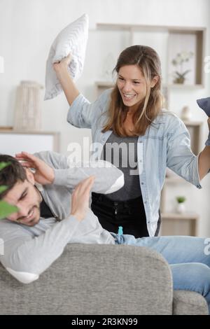 man and woman having a pillow fight on couch Stock Photo