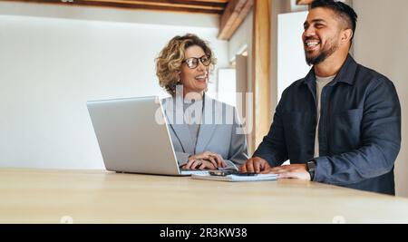 Happy business colleagues working together in an office. Two business people having a meeting about a project. Teamwork and collaboration between busi Stock Photo