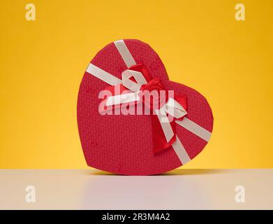 Red cardboard gift box in the shape of a heart on a yellow background Stock Photo