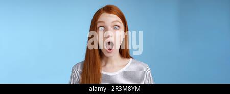Wow so cool. Impressed speechless amused attractive redhead girl blue eyes freckles open mouth wide omg drop jaw astonished expr Stock Photo