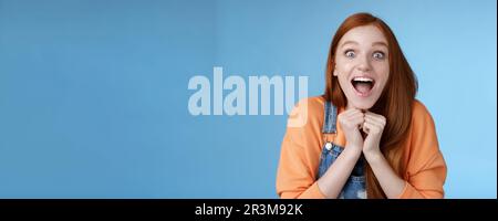 Cute redhead european girl blue eyes freckles reacting amused shocking rumor lift eyebrows drop jaw surprised smiling excited pi Stock Photo