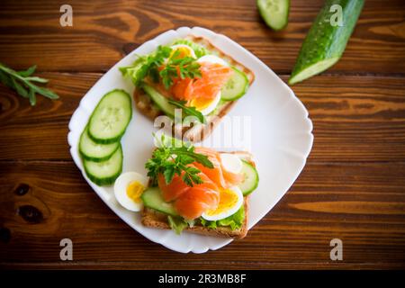 fried toast with lettuce, egg, cucumbers and red fish in a plate, on a wooden table. Stock Photo