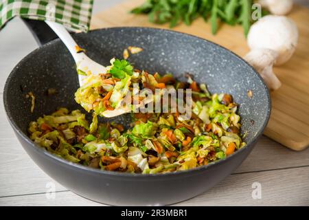 cabbage early fried with mushrooms, carrots and vegetables in a frying pan. Stock Photo
