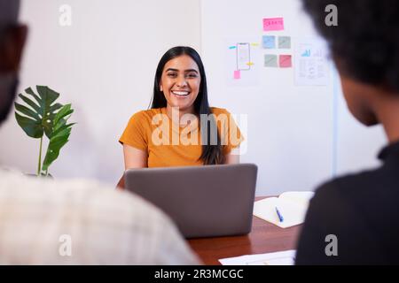 Young Indian woman smiles during team meeting, using laptop, scrum team Stock Photo