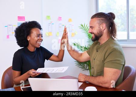 Two colleagues high five over final design of mobile app, developers coding UX Stock Photo