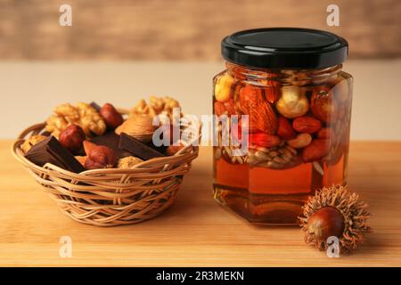 Different nuts with honey in jar and wicker basket with snacks on wooden table Stock Photo