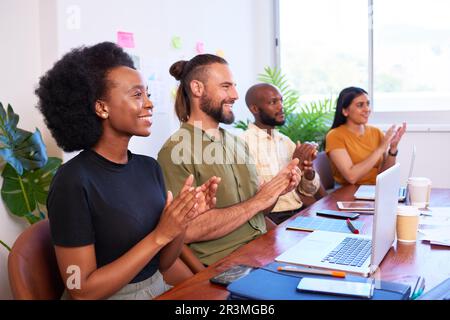 Four diverse team members clapping hands at meeting presentation, tech team Stock Photo