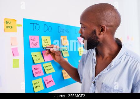 Black developer writes ticket on scrum board, sprint planning coding meeting Stock Photo