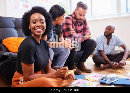 Portrait of female UX designer sitting on floor, creative brainstorm with team Stock Photo