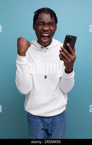 happy young african guy in white sweatshirt won online contest using smart phone Stock Photo