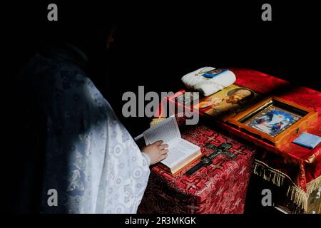 Hand of priest holds opened Holy Bible on the lectern near cross and icons for rite in Orthodox Ukrainian church. Top view. Stock Photo