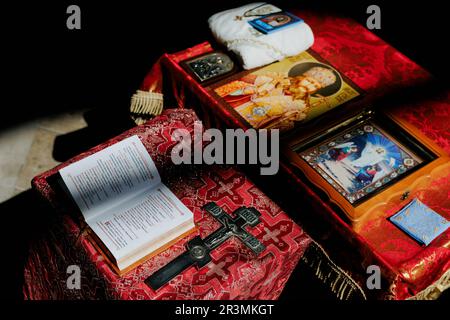 Opened Holy Bible is on the lectern near cross are against background of icons for rite in Orthodox Ukrainian church. Stock Photo
