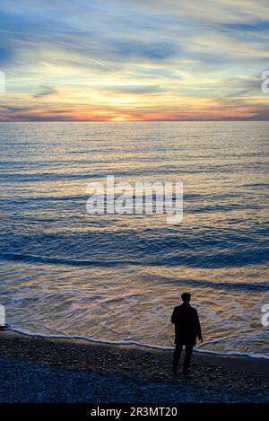 A man in a coat on the seashore at sunset Stock Photo