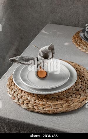Festive Easter table setting. Funny Easter bunny made of egg and linen napkin on plate. Gray background Stock Photo