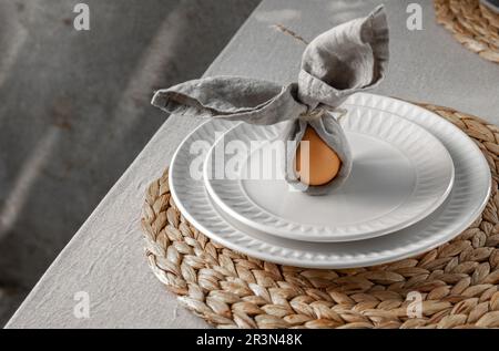 Festive Easter table setting. Funny Easter bunny made of egg and linen napkin on plate. Gray background Stock Photo