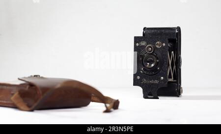 A vintage Zeiss Ikon Piccolette camera from the 1920s next to a vintage Kodak leather camera case on a clean white background Stock Photo