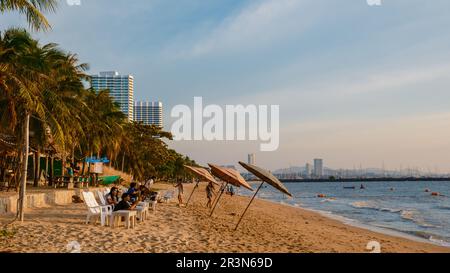 Sunset at a tropical beach with palm trees. Pattaya Thailand, people relaxing in front of a restaurant at the beach Stock Photo