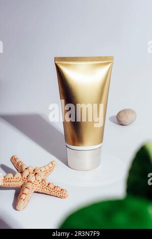 Golden cream tube and starfish on white background with hard shadows. Sunscreen, natural cosmetics concept. Closeup. Stock Photo