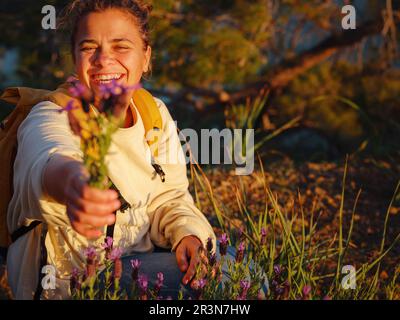 young caucasian woman collects a bouquet of broadleaf or French lavender , holds a wild flower bouquet in sunset light.. Flowers, grass meadow hill. G Stock Photo