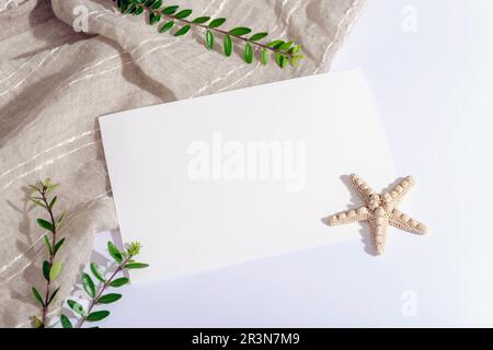 Blank paper sheet, starfish and green leaves on white table. Top view, flat lay, mockup. Stock Photo