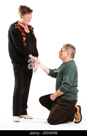 Senior Citizens: Renewing Vows. A senior man proposing to his smiling partner. Full length portrait, isolated on white. From a series. Stock Photo