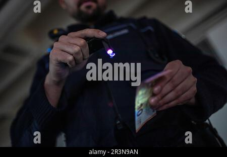 Stuttgart, Germany. 24th May, 2023. A police officer uses his new lamp to check the authenticity of a banknote, for example, with the help of UV light during an operation. The Southwest Police will be getting these new lamps for use from now on. Credit: Christoph Schmidt/dpa/Alamy Live News Stock Photo