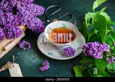 Tasty black tea in vintage white cup on mint green concrete table with aromatic lilac flowers Stock Photo
