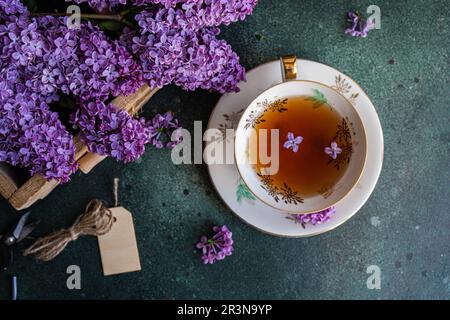 Tasty black tea in vintage white cup on mint green concrete table with aromatic lilac flowers Stock Photo
