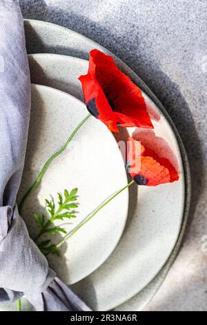 Summer table with red poppy flowers on a set of ceramic plates with a cloth napkin on top on a grey concrete background Stock Photo