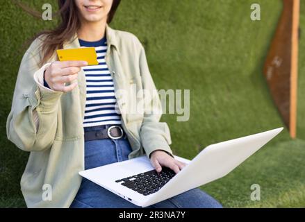 Unrecognizable young female freelancer browsing laptop with credit card while making online payment on internet in street Stock Photo